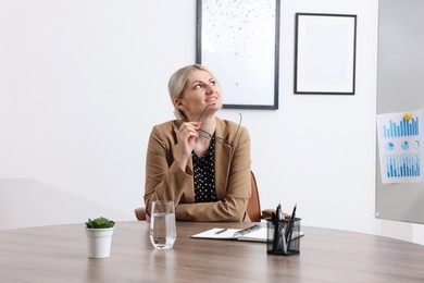 Photo of Dreams come true. Woman with glasses thinking about something at wooden table indoors