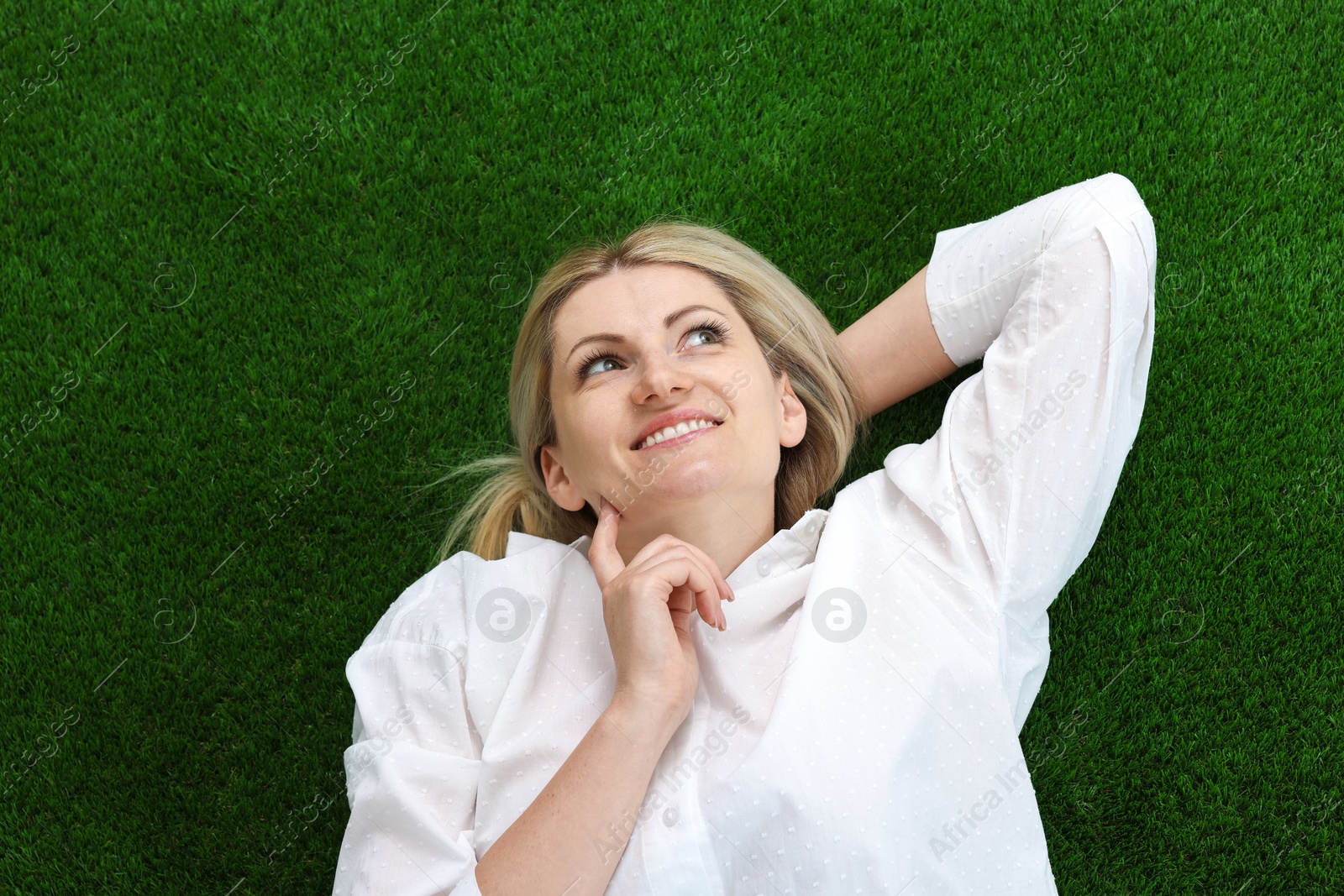 Dreams come true. Woman thinking about something on green grass outdoors, top view Photo of Dreams come true. Woman thinking about something on green grass outdoors, top view