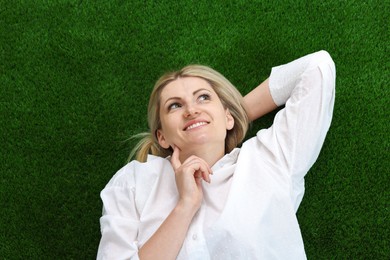Photo of Dreams come true. Woman thinking about something on green grass outdoors, top view