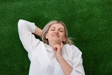 Photo of Dreams come true. Woman thinking about something on green grass outdoors, top view