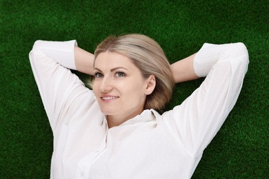 Photo of Dreams come true. Woman thinking about something on green grass outdoors, top view