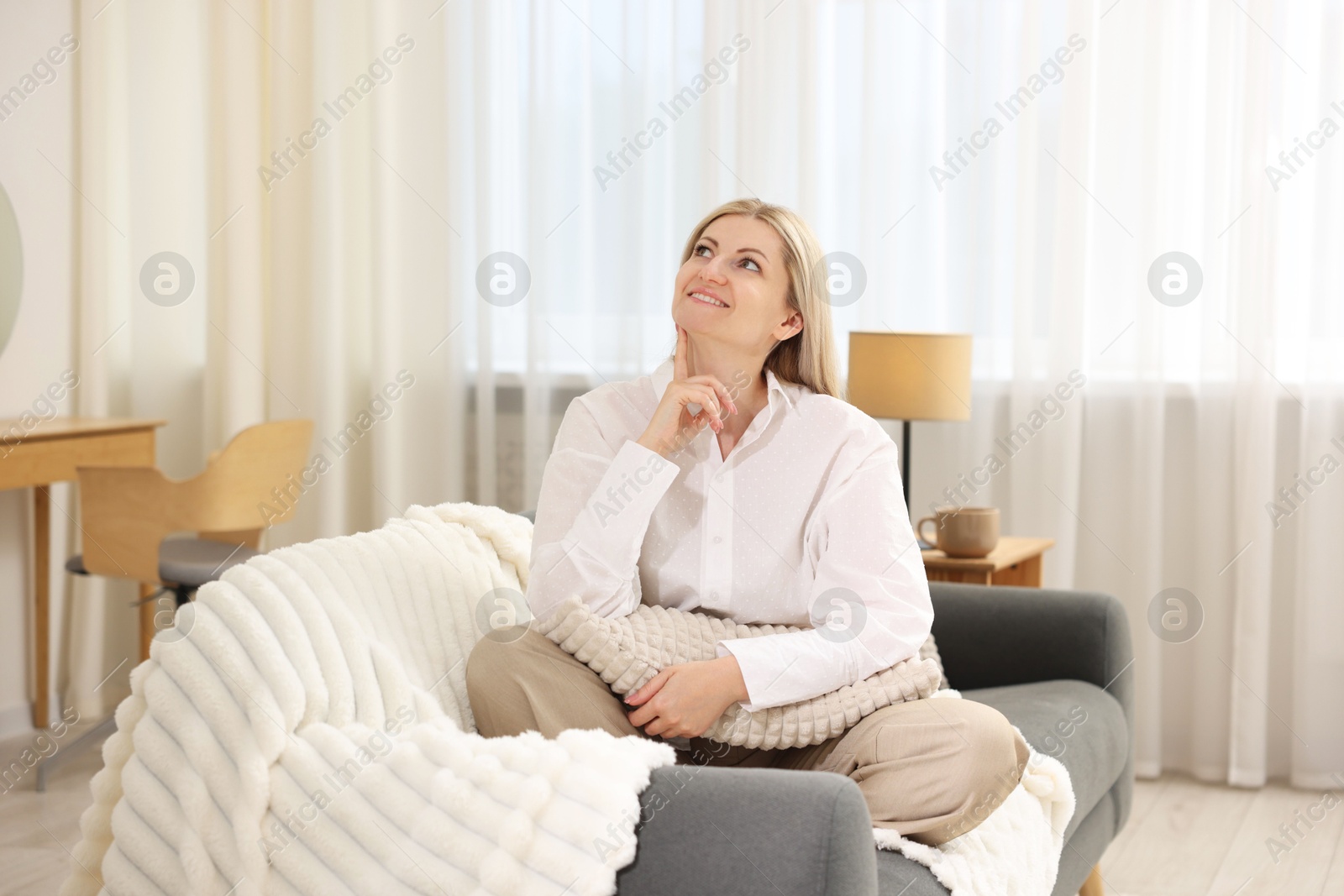 Dreams come true. Woman with pillow thinking about something on sofa at home Photo of Dreams come true. Woman with pillow thinking about something on sofa at home