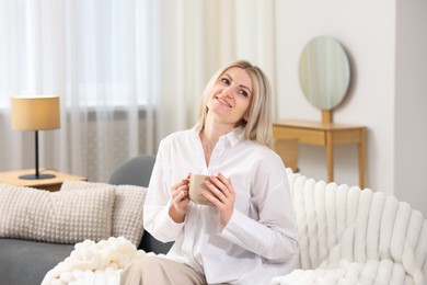 Photo of Dreams come true. Woman with cup of drink thinking about something on sofa at home
