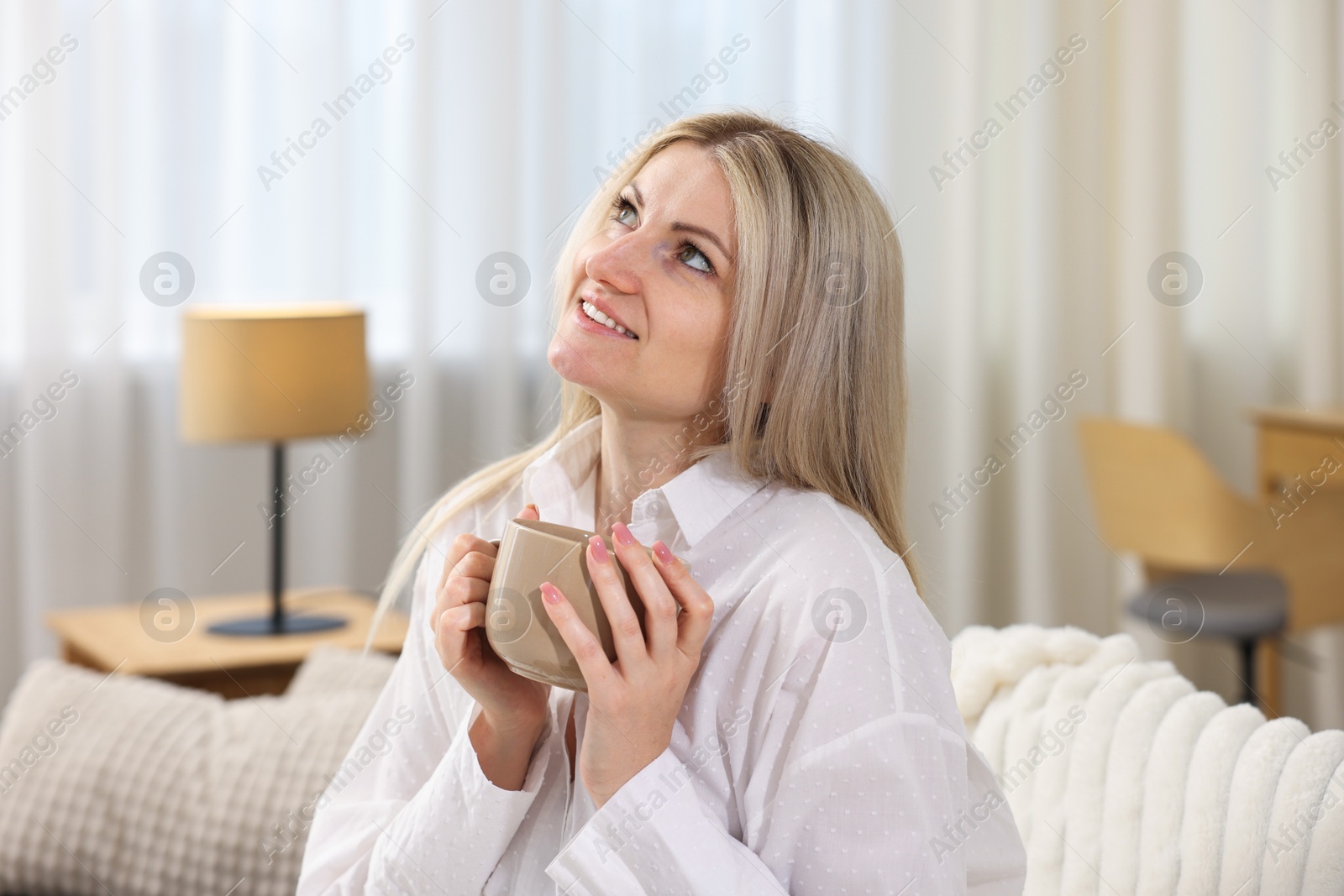 Dreams come true. Woman with cup of drink thinking about something on sofa at home Photo of Dreams come true. Woman with cup of drink thinking about something on sofa at home