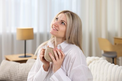 Photo of Dreams come true. Woman with cup of drink thinking about something on sofa at home