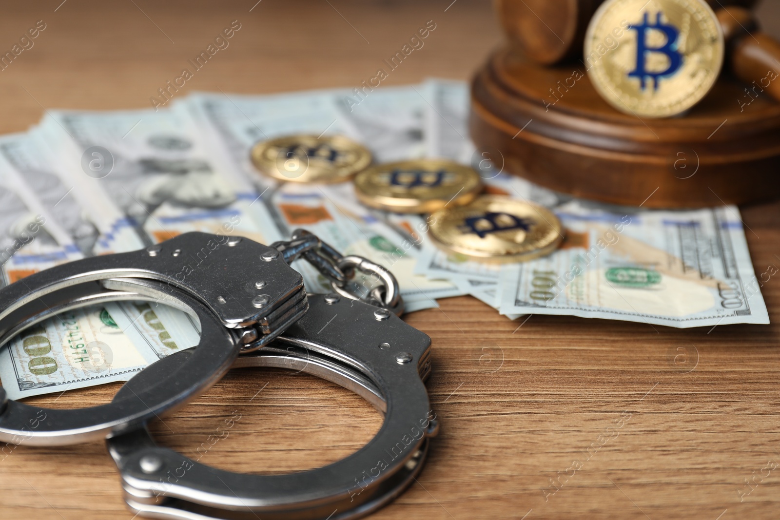 Photo of Cryptocurrency. Bitcoins, handcuffs, dollars and judge's gavel on wooden table, closeup