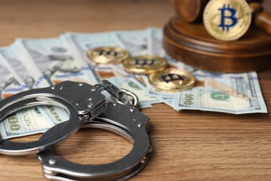 Photo of Cryptocurrency. Bitcoins, handcuffs, dollars and judge's gavel on wooden table, closeup