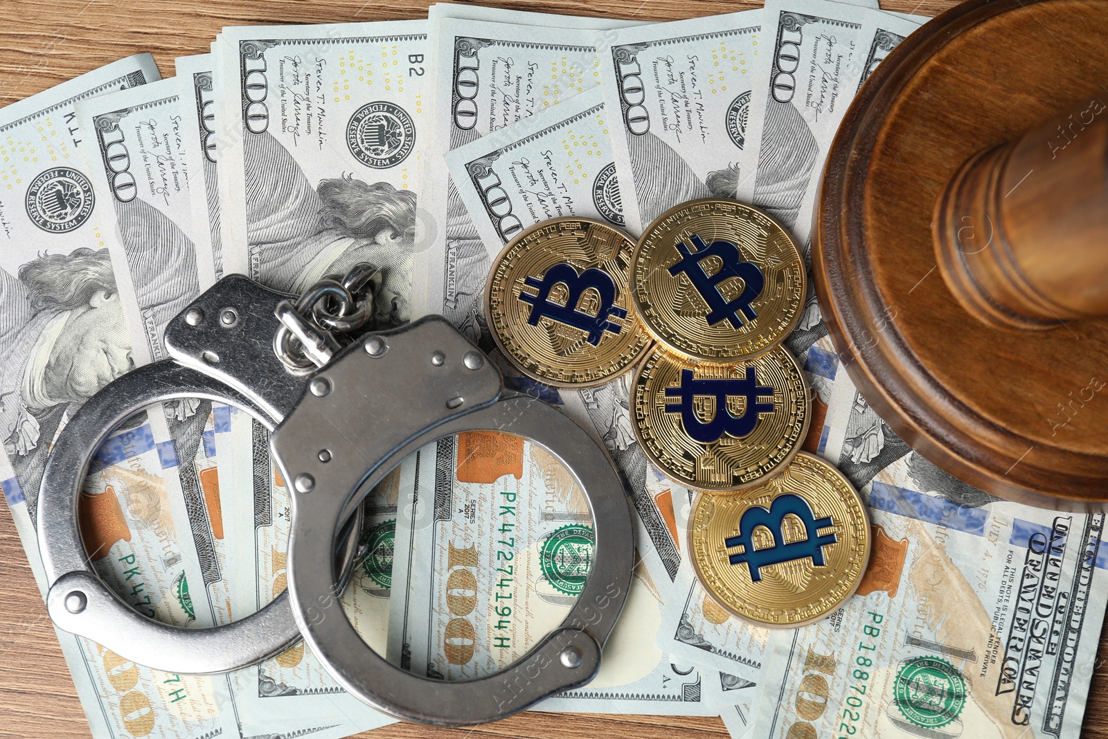 Photo of Cryptocurrency. Bitcoins, handcuffs, dollars and judge's gavel on wooden table, flat lay