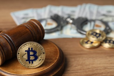 Photo of Cryptocurrency. Bitcoins, judge's gavel, handcuffs and dollars on wooden table, closeup