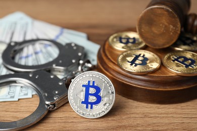 Photo of Cryptocurrency. Bitcoins, judge's gavel, handcuffs and dollars on wooden table, closeup