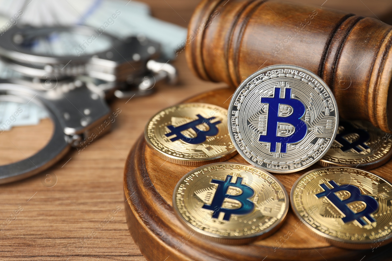 Photo of Cryptocurrency. Bitcoins, judge's gavel, handcuffs and dollars on wooden table, closeup