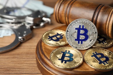 Photo of Cryptocurrency. Bitcoins, judge's gavel, handcuffs and dollars on wooden table, closeup