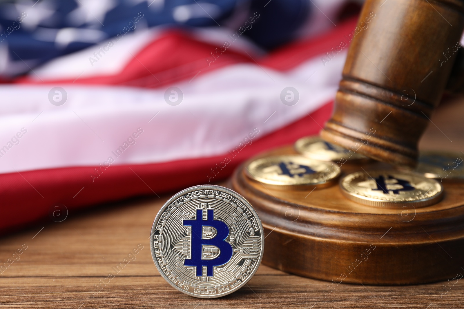 Photo of Cryptocurrency. Bitcoins, judge's gavel and American flag on wooden table, closeup