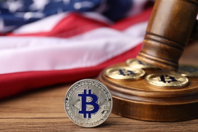 Photo of Cryptocurrency. Bitcoins, judge's gavel and American flag on wooden table, closeup