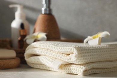 Photo of Clean waffle towel, plumeria flowers and cosmetic products on counter in bathroom, closeup