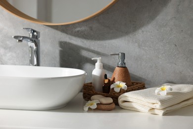 Photo of Clean waffle towel, plumeria flowers and cosmetic products on counter in bathroom