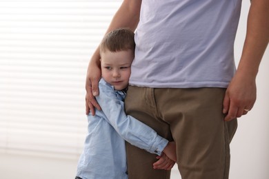 Photo of Little boy clinging to his father indoors. Separation anxiety