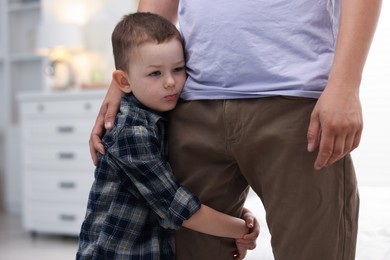 Photo of Little boy clinging to his father indoors. Separation anxiety