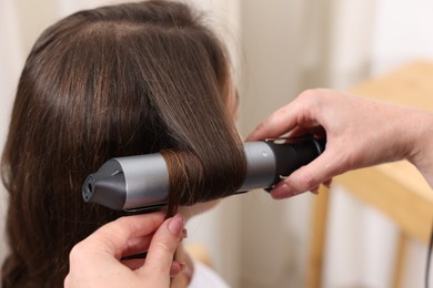Photo of Hairdresser curling woman's hair in salon, closeup