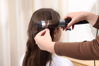 Photo of Hairdresser curling woman's hair in salon, closeup