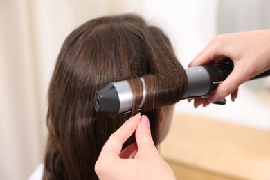 Photo of Hairdresser curling woman's hair in salon, closeup
