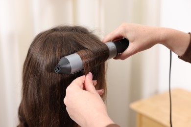 Photo of Hairdresser curling woman's hair in salon, closeup