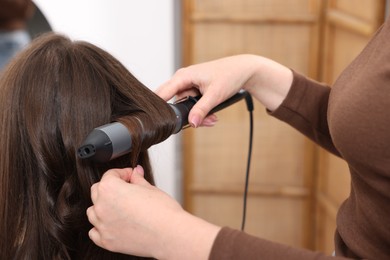 Photo of Hairdresser curling woman's hair in salon, closeup