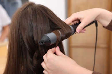 Photo of Hairdresser curling woman's hair in salon, closeup