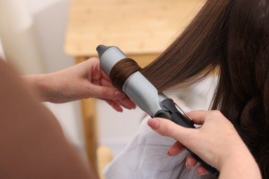 Photo of Hairdresser curling woman's hair in salon, closeup