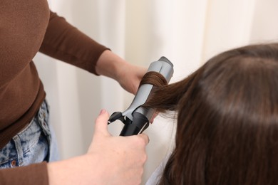 Photo of Hairdresser curling woman's hair in salon, closeup