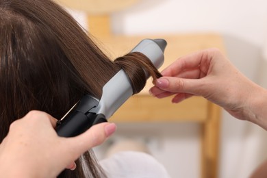 Photo of Hairdresser curling woman's hair in salon, closeup