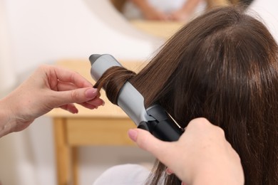 Photo of Hairdresser curling woman's hair in salon, closeup