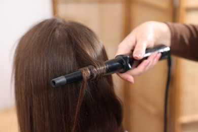 Photo of Hairdresser curling woman's hair in salon, closeup