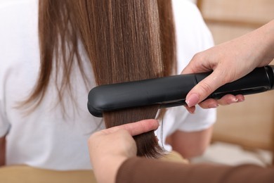 Photo of Hairdresser straightening woman's hair with flat iron in salon, closeup
