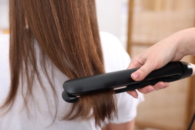 Photo of Hairdresser straightening woman's hair with flat iron in salon, closeup