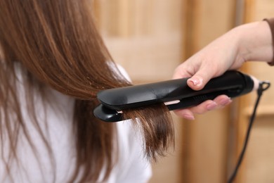 Photo of Hairdresser straightening woman's hair with flat iron in salon, closeup