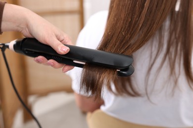 Photo of Hairdresser straightening woman's hair with flat iron in salon, closeup