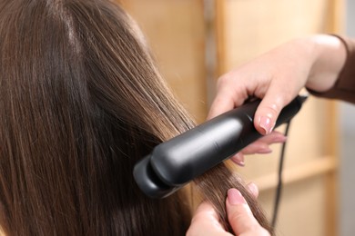 Photo of Hairdresser straightening woman's hair with flat iron in salon, closeup