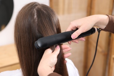 Photo of Hairdresser straightening woman's hair with flat iron in salon, closeup