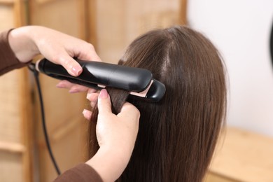 Photo of Hairdresser straightening woman's hair with flat iron in salon, closeup