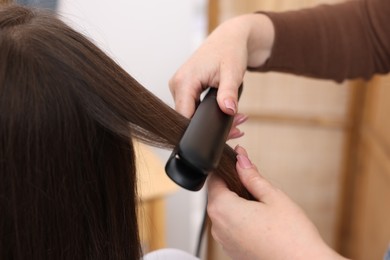 Photo of Hairdresser straightening woman's hair with flat iron in salon, closeup