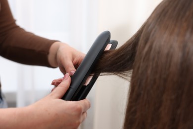 Photo of Hairdresser straightening woman's hair with flat iron in salon, closeup