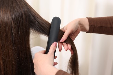 Photo of Hairdresser straightening woman's hair with flat iron in salon, closeup