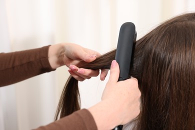 Photo of Hairdresser straightening woman's hair with flat iron in salon, closeup