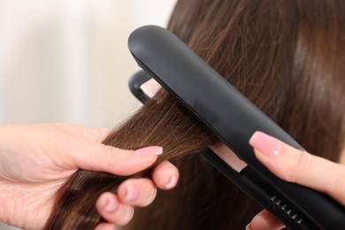 Photo of Hairdresser straightening woman's hair with flat iron in salon, closeup