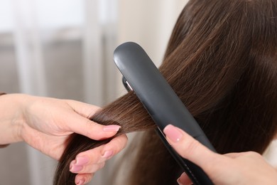 Photo of Hairdresser straightening woman's hair with flat iron in salon, closeup