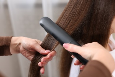 Photo of Hairdresser straightening woman's hair with flat iron in salon, closeup