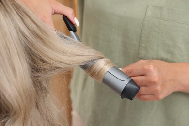 Photo of Hairdresser curling woman's hair in salon, closeup