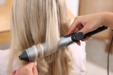 Photo of Hairdresser curling woman's hair in salon, closeup