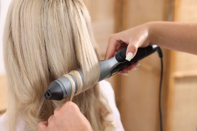 Photo of Hairdresser curling woman's hair in salon, closeup